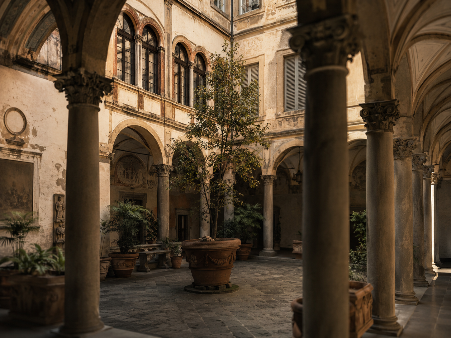Cortile interno di un palazzo storico fiorentino con colonne, archi in pietra, pareti antiche e luce naturale calda che illumina piante e dettagli architettonici.